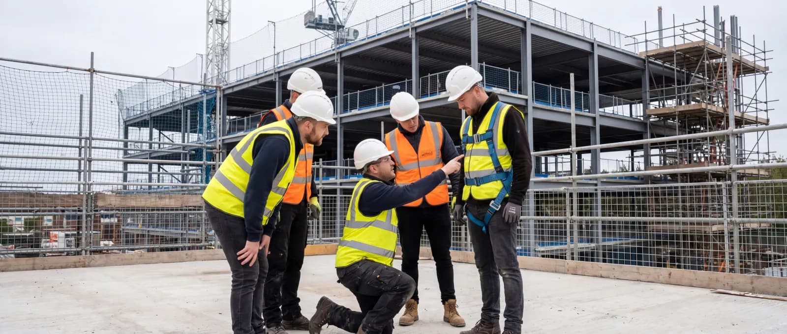 Construction workers conducting hands-on fall protection harness training at an active building site